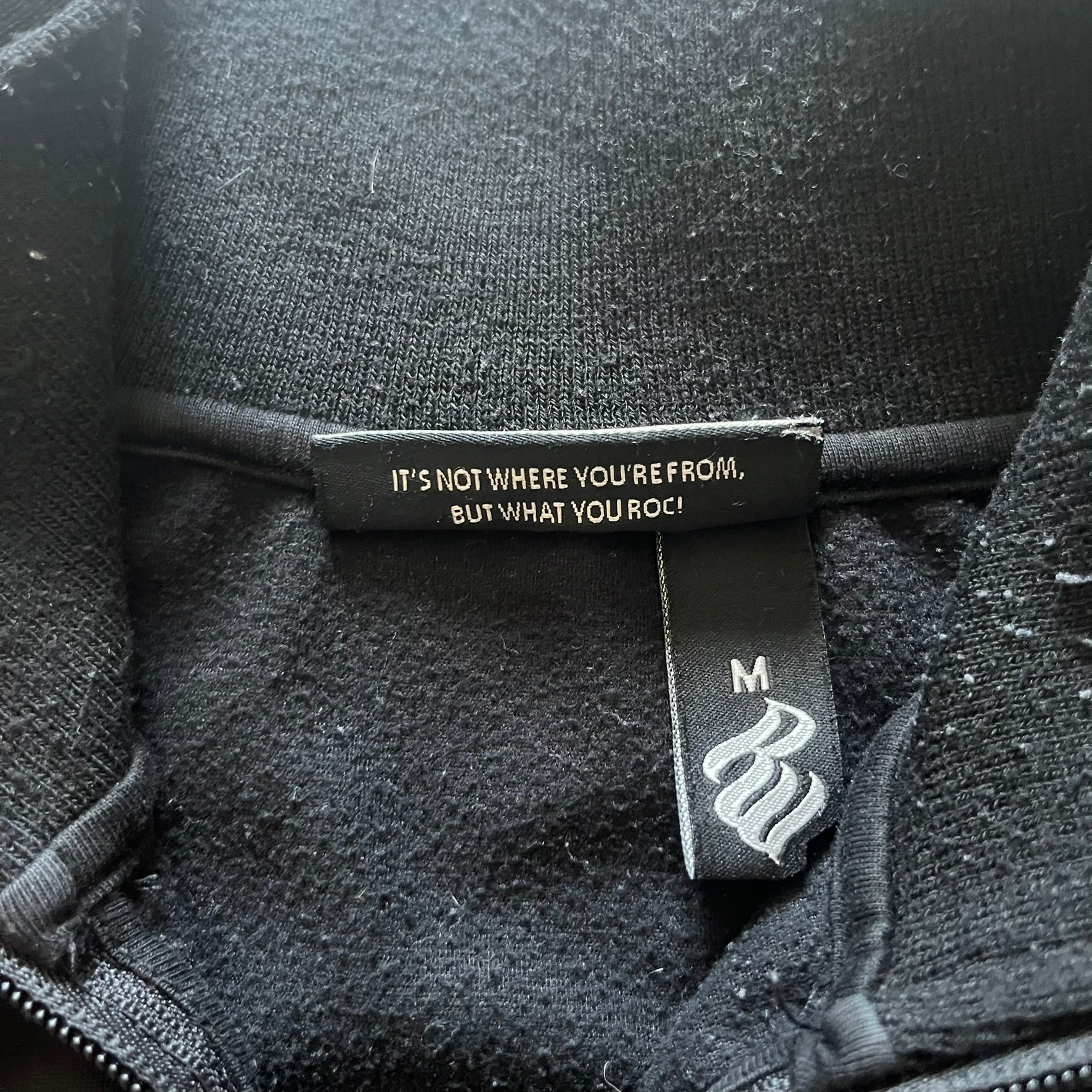 Vintage Rocawear black track jacket featuring a small embroidered chest logo and big white branding across the back. Silver zipper and wrist emblem add refined details to this early-2000s streetwear classic.