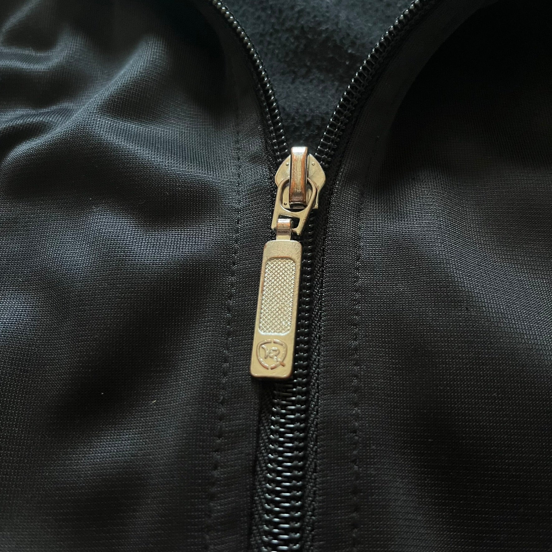 Vintage Rocawear black track jacket featuring a small embroidered chest logo and big white branding across the back. Silver zipper and wrist emblem add refined details to this early-2000s streetwear classic.