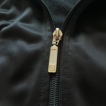 Vintage Rocawear black track jacket featuring a small embroidered chest logo and big white branding across the back. Silver zipper and wrist emblem add refined details to this early-2000s streetwear classic.