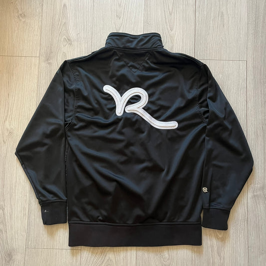 Rocawear black track jacket in size large, designed with a small embroidered logo on the chest and a large white logo across the back. A silver emblem near the wrist and a detailed silver zipper add distinctive touches. A sleek early 2000s streetwear piece.