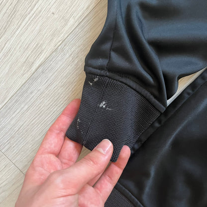 Rocawear black track jacket in size large, designed with a small embroidered logo on the chest and a large white logo across the back. A silver emblem near the wrist and a detailed silver zipper add distinctive touches. A sleek early 2000s streetwear piece.