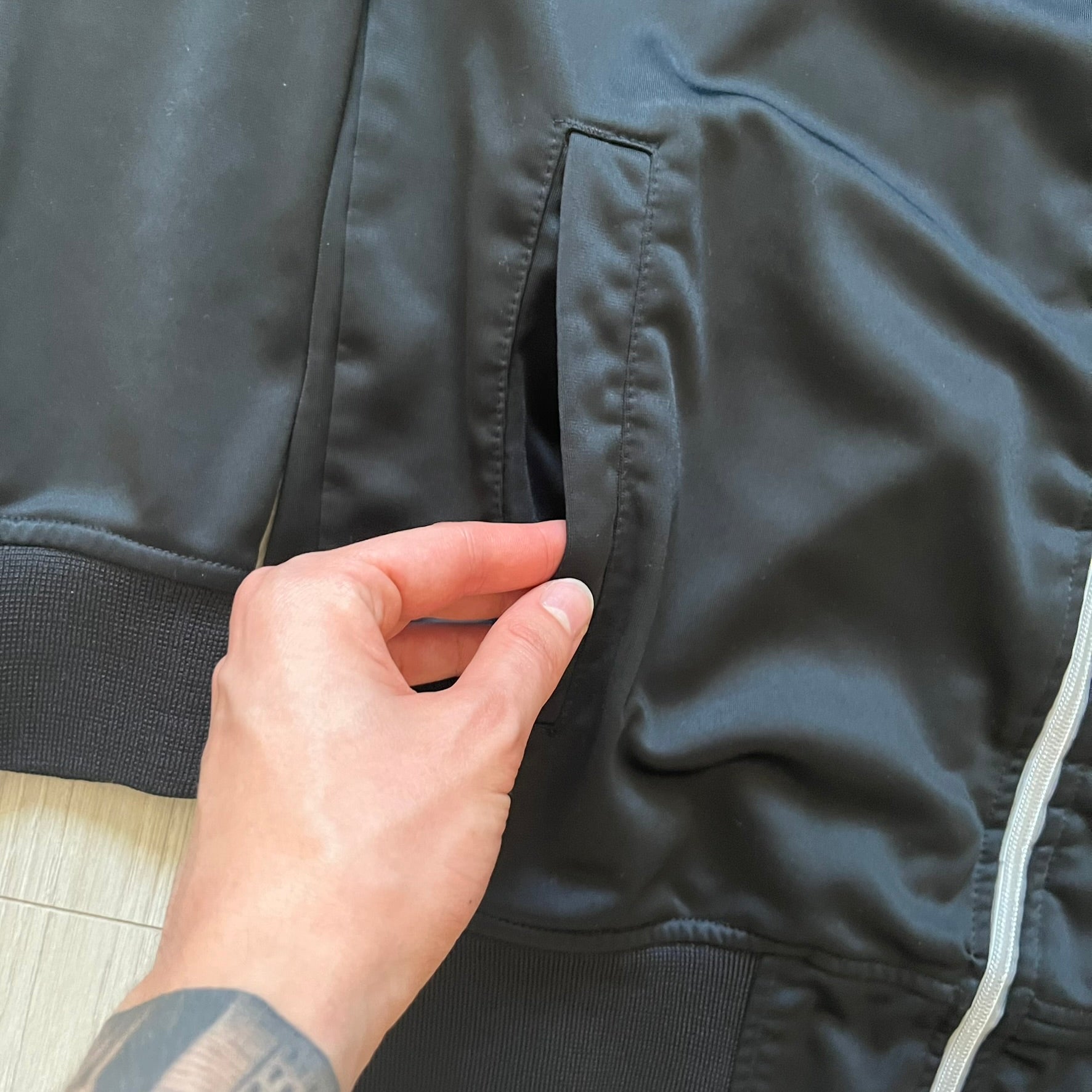 Rocawear black track jacket in size large, designed with a small embroidered logo on the chest and a large white logo across the back. A silver emblem near the wrist and a detailed silver zipper add distinctive touches. A sleek early 2000s streetwear piece.