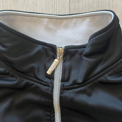 Rocawear black track jacket in size large, designed with a small embroidered logo on the chest and a large white logo across the back. A silver emblem near the wrist and a detailed silver zipper add distinctive touches. A sleek early 2000s streetwear piece.