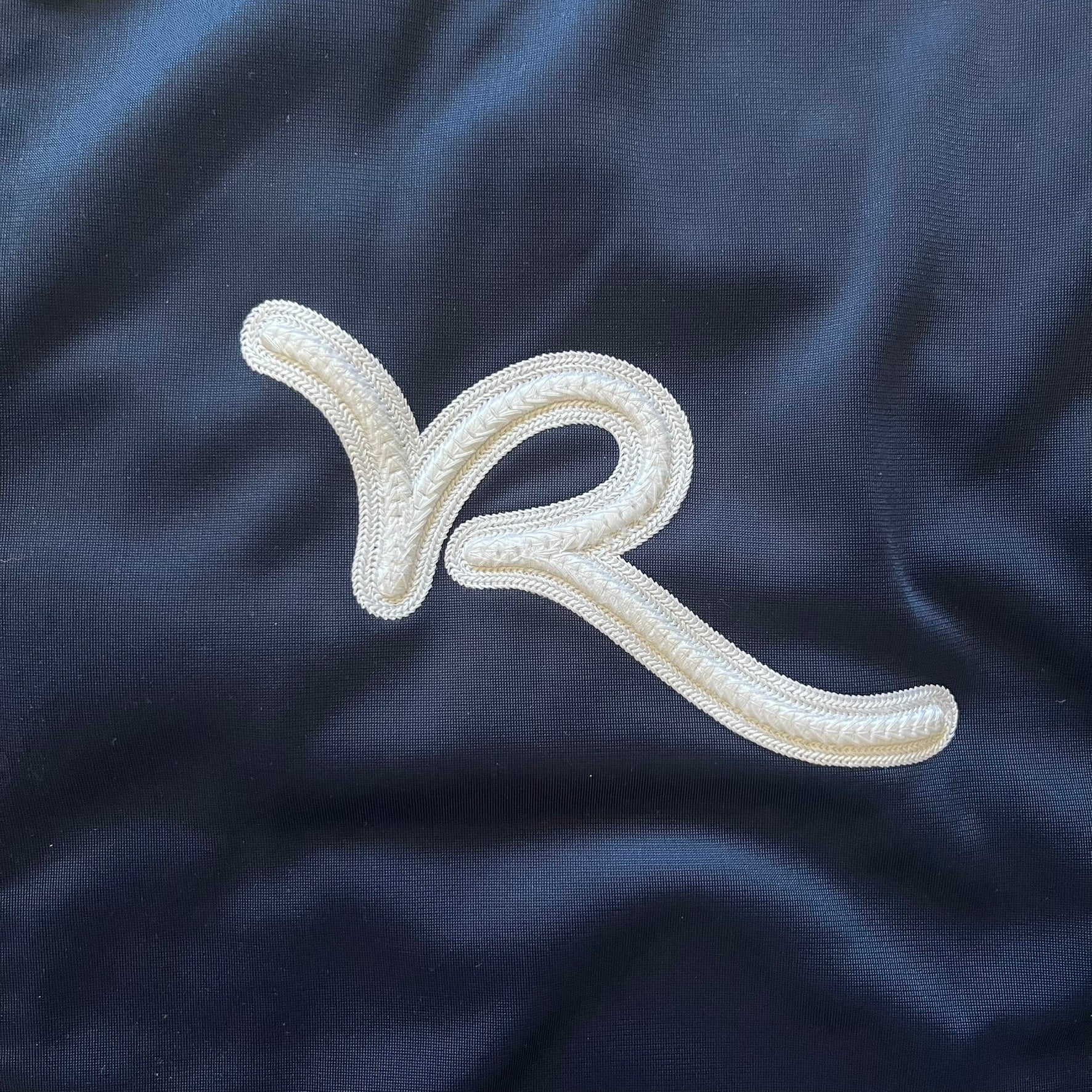 Rocawear Dark Navy Vintage Track Jacket, featuring a small embroidered logo on the chest and a large white logo across the back, finished with a silver emblem near the wrist and a detailed silver zipper.