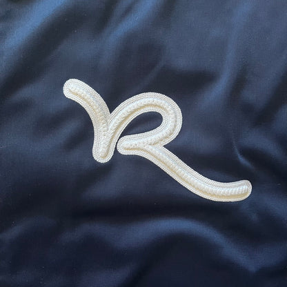 Rocawear Dark Navy Vintage Track Jacket, featuring a small embroidered logo on the chest and a large white logo across the back, finished with a silver emblem near the wrist and a detailed silver zipper.