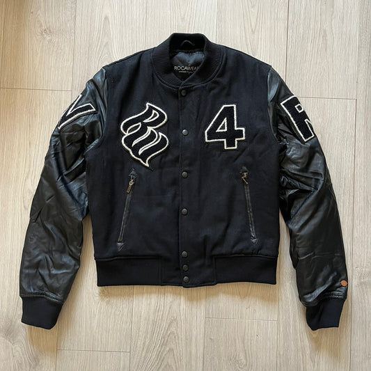 Rocawear black bomber jacket detailed with multiple statement patches, including “R” and “W” on the shoulders, a Rocawear logo with a “4” on the chest, and a large text logo across the back. Crafted with great detailing, it reflects the brand’s early 2000s streetwear identity.