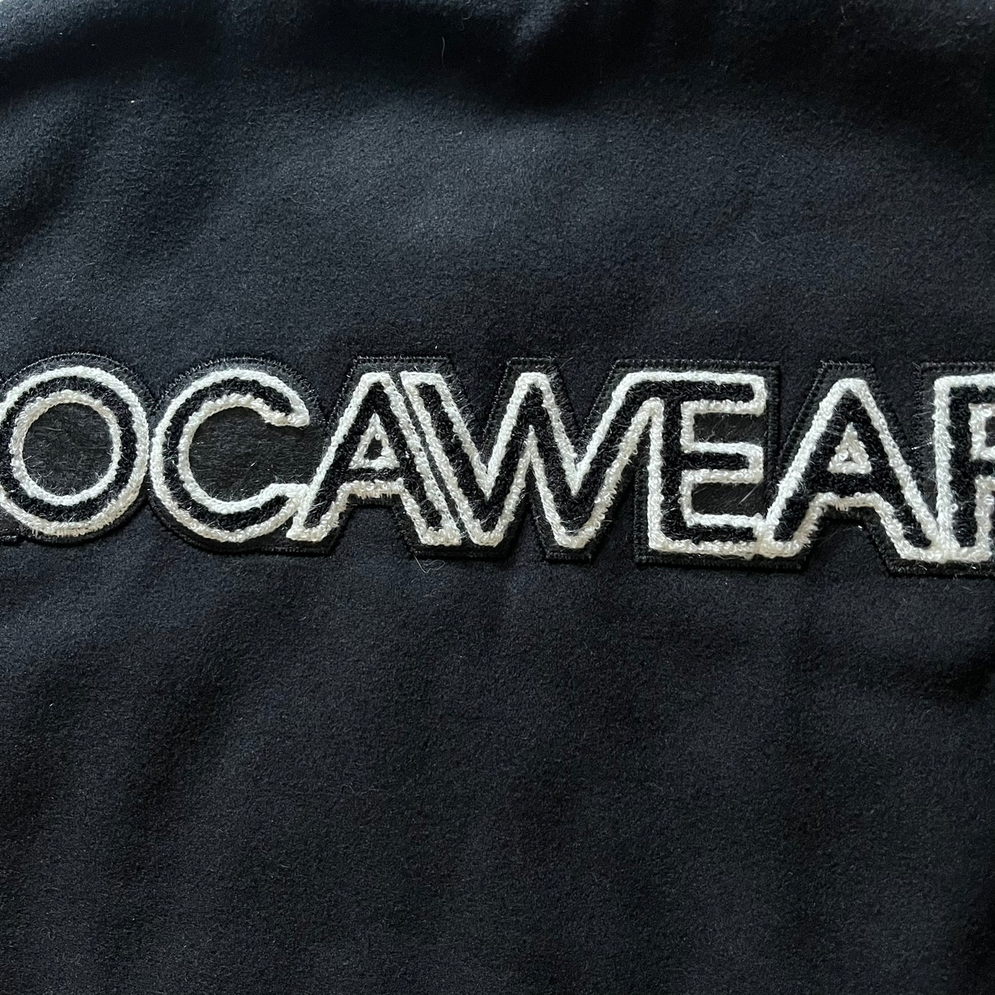 Rocawear black bomber jacket detailed with multiple statement patches, including “R” and “W” on the shoulders, a Rocawear logo with a “4” on the chest, and a large text logo across the back. Crafted with great detailing, it reflects the brand’s early 2000s streetwear identity.
