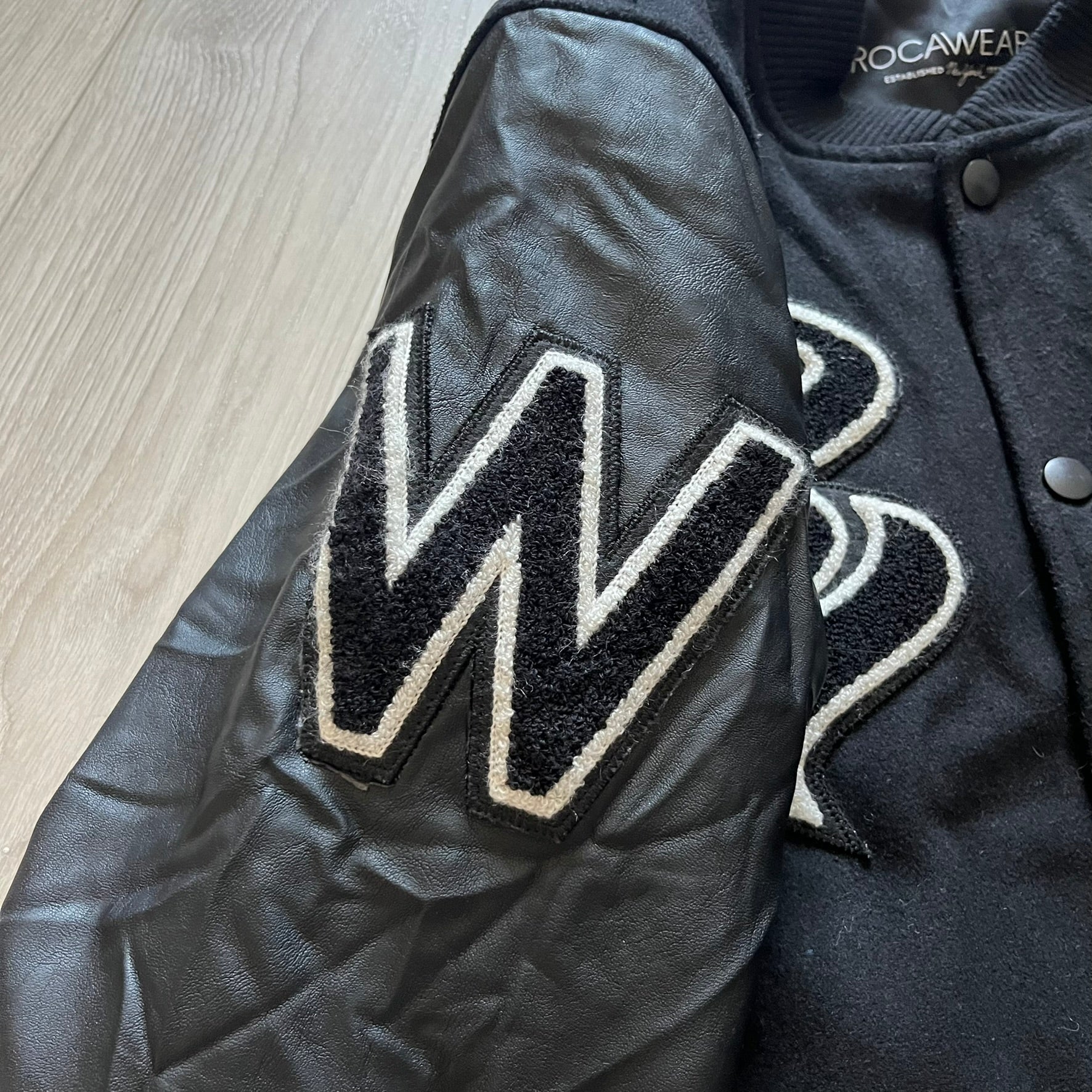 Rocawear black bomber jacket detailed with multiple statement patches, including “R” and “W” on the shoulders, a Rocawear logo with a “4” on the chest, and a large text logo across the back. Crafted with great detailing, it reflects the brand’s early 2000s streetwear identity.