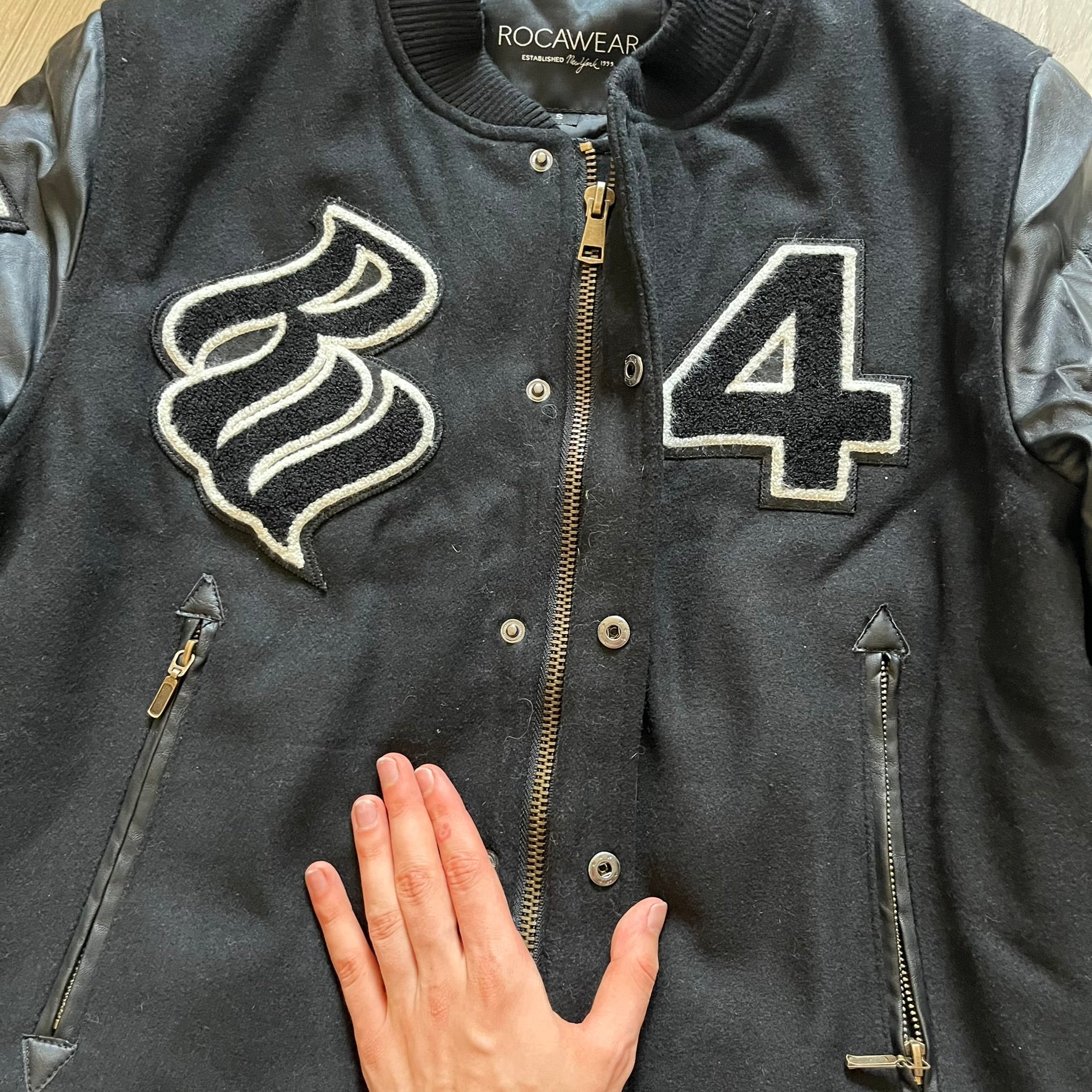 Rocawear black bomber jacket detailed with multiple statement patches, including “R” and “W” on the shoulders, a Rocawear logo with a “4” on the chest, and a large text logo across the back. Crafted with great detailing, it reflects the brand’s early 2000s streetwear identity.