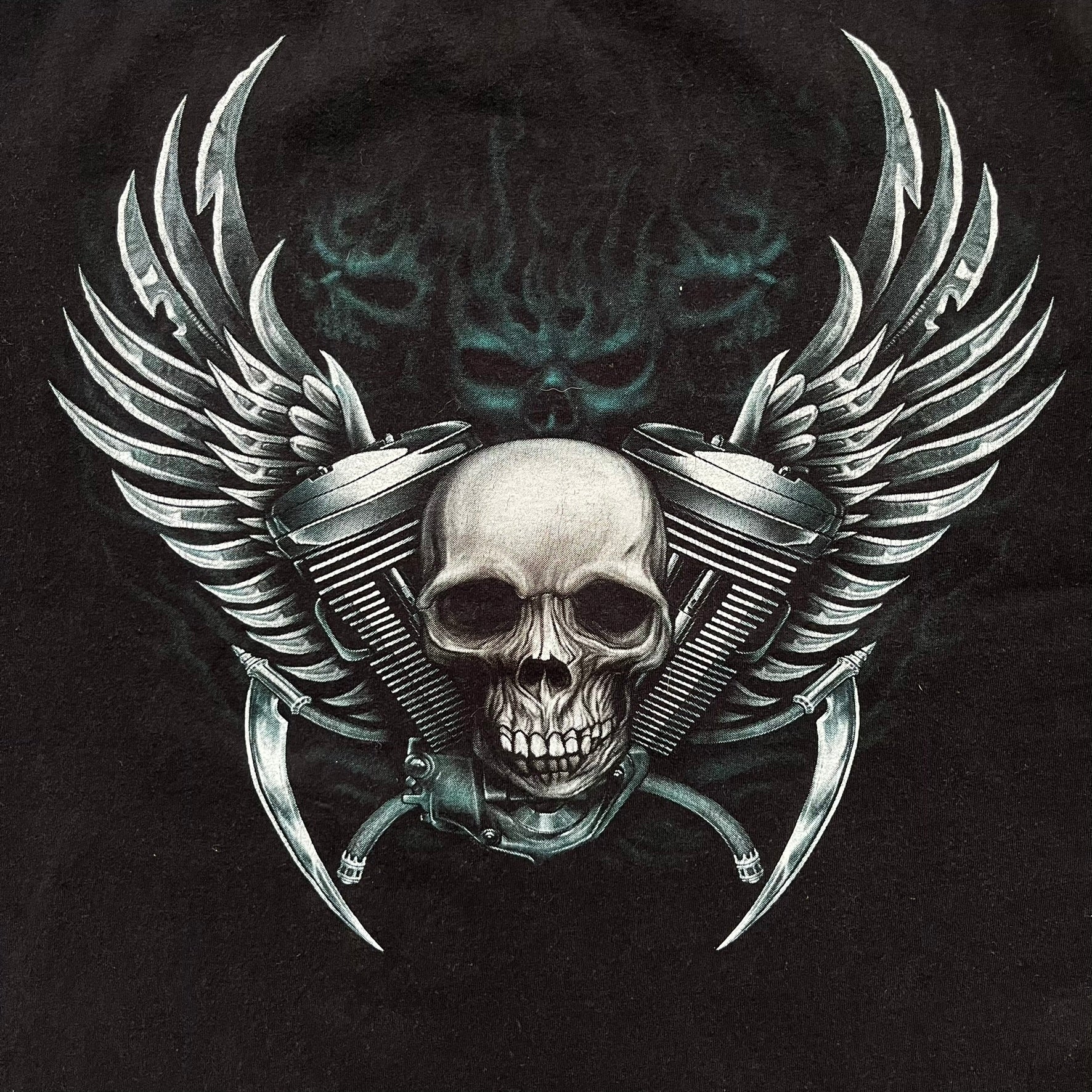 Rock Eagle 2010s Skull Biker Tee is a black T-shirt featuring a large front graphic of a skull-faced biker riding a motorcycle while being chased by a skeletal Grim Reaper holding a scythe. The artwork includes lightning strikes, skulls, and detailed airbrush-style effects throughout the scene. The back features a graphic of a winged engine with a skull at the center. Finished with a Rock Eagle neck tag.
