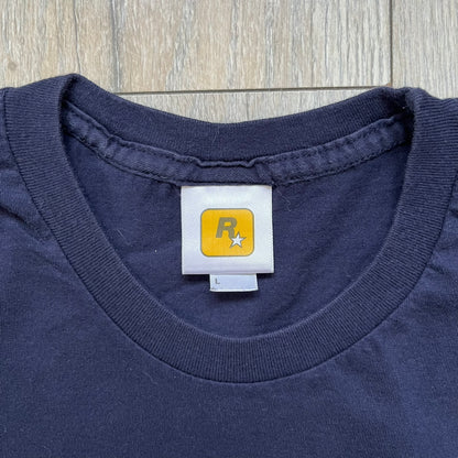 Rockstar Games 'Canis Canem Edit (Bully)' Navy Tee is a dark navy T-shirt made in the USA featuring a yellow "Canis Canem Edit" text on the chest, referencing the original Bully game title. The back displays a large yellow Bullworth Academy logo, while a small yellow Rockstar logo is printed on the sleeve. The shirt includes an official Rockstar Games neck tag.