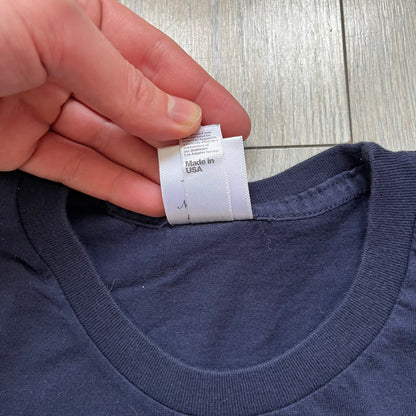 Rockstar Games 'Canis Canem Edit (Bully)' Navy Tee is a dark navy T-shirt made in the USA featuring a yellow "Canis Canem Edit" text on the chest, referencing the original Bully game title. The back displays a large yellow Bullworth Academy logo, while a small yellow Rockstar logo is printed on the sleeve. The shirt includes an official Rockstar Games neck tag.