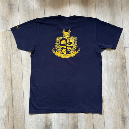 Rockstar Games 'Canis Canem Edit (Bully)' Navy Tee is a dark navy T-shirt made in the USA featuring a yellow "Canis Canem Edit" text on the chest, referencing the original Bully game title. The back displays a large yellow Bullworth Academy logo, while a small yellow Rockstar logo is printed on the sleeve. The shirt includes an official Rockstar Games neck tag.