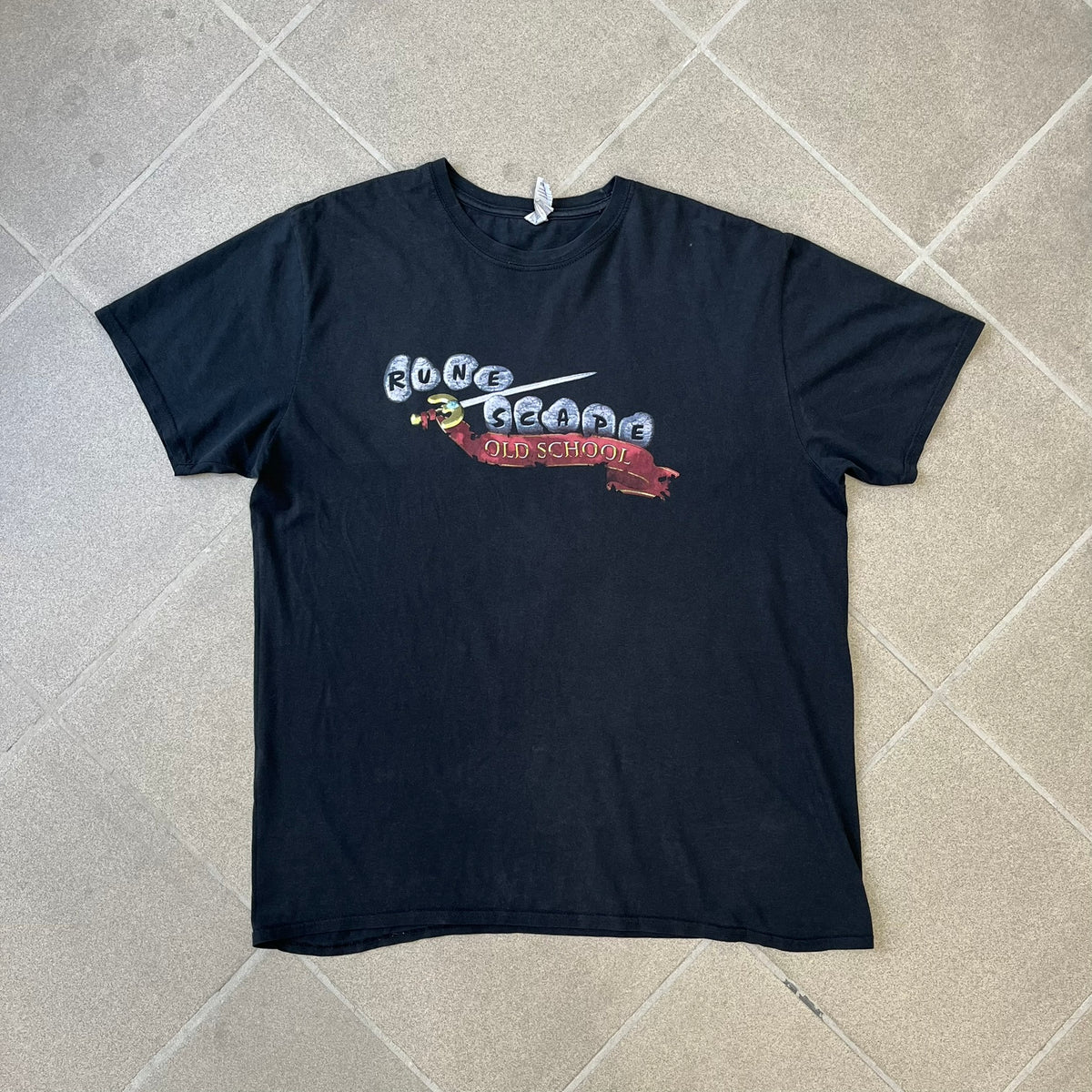 RuneScape Old School 2010's Logo Tee features a black construction with the RuneScape Old School logo printed on the front. The shirt was available through the official Jagex store and dates from the late 2010s to 2020s. Made on a Gildan blank.
