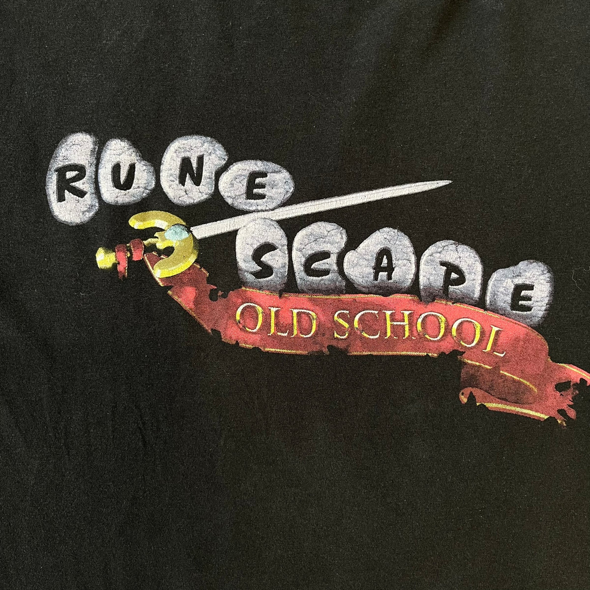 RuneScape Old School 2010's Logo Tee features a black construction with the RuneScape Old School logo printed on the front. The shirt was available through the official Jagex store and dates from the late 2010s to 2020s. Made on a Gildan blank.
