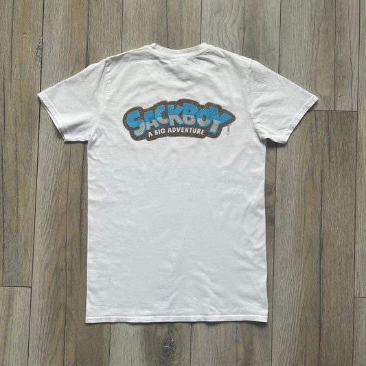 Sackboy: A Big Adventure 2020 White Promo Tee is a white cotton T-shirt featuring official Sony licensing and a “not for sale” internal tag. The front includes a small printed faux chest pocket design with Sackboy waving from inside it. The upper back displays a large “Sackboy: A Big Adventure” game logo print.