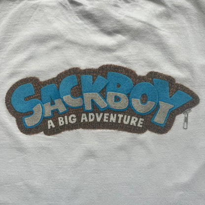 Sackboy: A Big Adventure 2020 White Promo Tee is a white cotton T-shirt featuring official Sony licensing and a “not for sale” internal tag. The front includes a small printed faux chest pocket design with Sackboy waving from inside it. The upper back displays a large “Sackboy: A Big Adventure” game logo print.