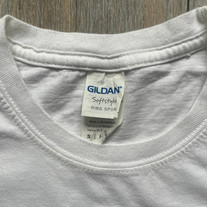Sackboy: A Big Adventure 2020 White Promo Tee is a white cotton T-shirt featuring official Sony licensing and a “not for sale” internal tag. The front includes a small printed faux chest pocket design with Sackboy waving from inside it. The upper back displays a large “Sackboy: A Big Adventure” game logo print.