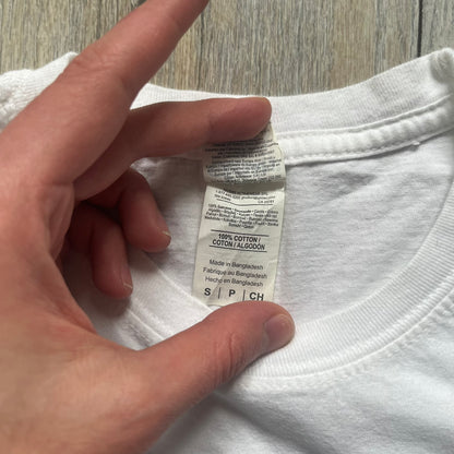 Sackboy: A Big Adventure 2020 White Promo Tee is a white cotton T-shirt featuring official Sony licensing and a “not for sale” internal tag. The front includes a small printed faux chest pocket design with Sackboy waving from inside it. The upper back displays a large “Sackboy: A Big Adventure” game logo print.