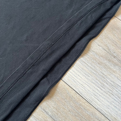 Saint Laurent 2018 Black Logo Tee is a black short-sleeve T-shirt made in Italy from 100% cotton. The chest features a small logo print with white “Saint,” a red square, and white “Laurent” detailing. The shirt has a slightly elongated front hem compared to the back.