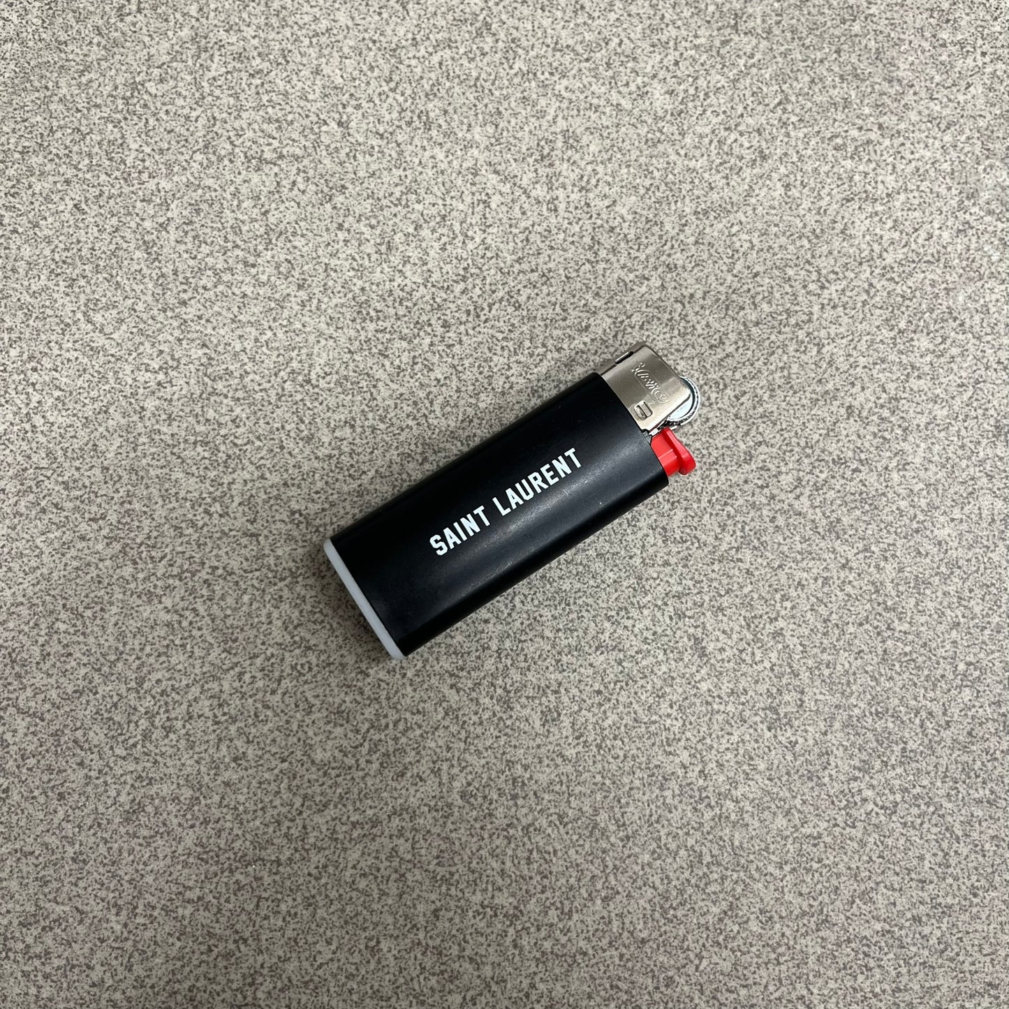 Saint Laurent Black 213 Saint-Honore Lighter is a black BIC gas lighter featuring white Saint Laurent branding on one side and 213 Saint-Honore Paris on the other side. It is an in-store-only item made in Spain.
