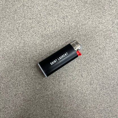 Saint Laurent Black 213 Saint-Honore Lighter is a black BIC gas lighter featuring white Saint Laurent branding on one side and 213 Saint-Honore Paris on the other side. It is an in-store-only item made in Spain.
