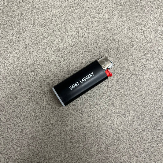 Saint Laurent Black 213 Saint-Honore Lighter is a black BIC gas lighter featuring white Saint Laurent branding on one side and 213 Saint-Honore Paris on the other side. It is an in-store-only item made in Spain.
