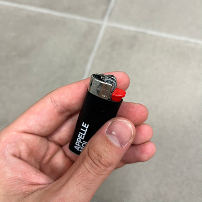 Saint Laurent Black 213 Saint-Honore Lighter is a black BIC gas lighter featuring white Saint Laurent branding on one side and Appelle Moi text on the other. It is an in-store-only item made in Spain.
