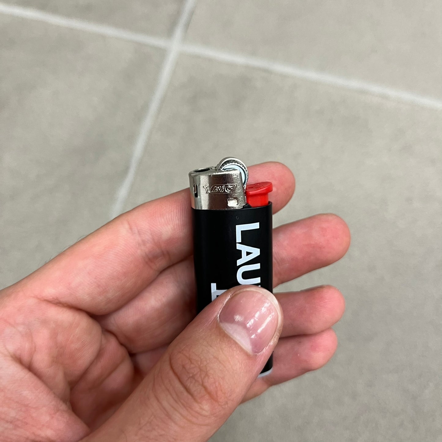 Saint Laurent Black Logo Lighter is a white BIC gas lighter featuring white Saint Laurent branding, with “Saint” printed above and “Laurent” mirrored underneath. It is an in-store-only item made in Spain. 