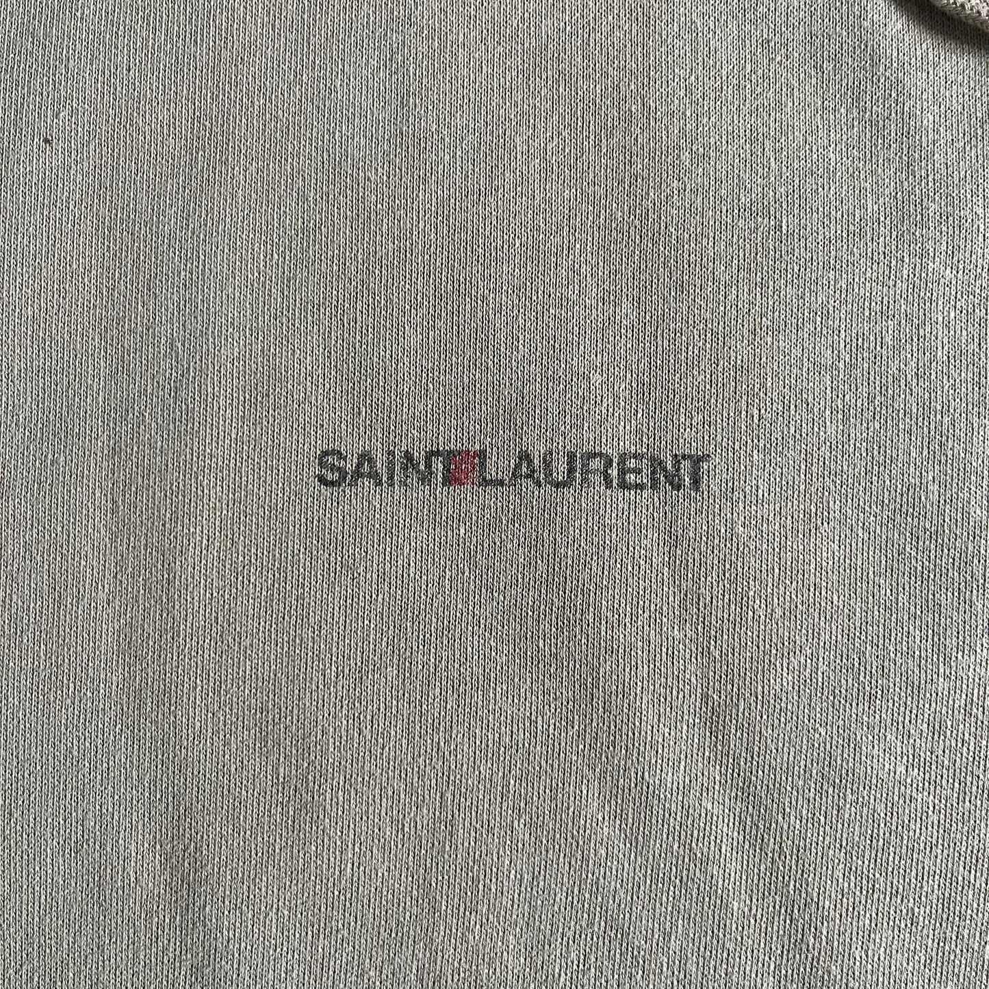Crafted in France from 100% cotton, this Saint Laurent Beige Hoodie features a minimalist aesthetic with the brand’s signature small Saint Laurent chest logo and red square detail. Designed with a classic front pocket and clean drawstrings without metal tips, it delivers understated Parisian luxury in a neutral tone.