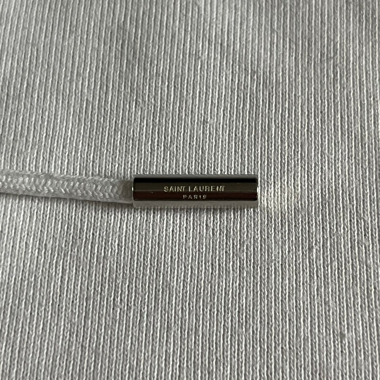 Saint Laurent Small Logo White Hoodie made in France from 100% cotton. Features a minimalist chest logo with “Saint” and “Laurent” separated by a small red square, silver-tipped drawstrings engraved with branding, and a classic front pocket. Designed with the brand’s signature minimalist aesthetic.