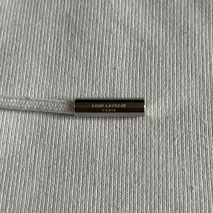 Saint Laurent Small Logo White Hoodie made in France from 100% cotton. Features a minimalist chest logo with “Saint” and “Laurent” separated by a small red square, silver-tipped drawstrings engraved with branding, and a classic front pocket. Designed with the brand’s signature minimalist aesthetic.