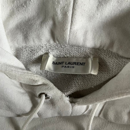 Saint Laurent Small Logo White Hoodie made in France from 100% cotton. Features a minimalist chest logo with “Saint” and “Laurent” separated by a small red square, silver-tipped drawstrings engraved with branding, and a classic front pocket. Designed with the brand’s signature minimalist aesthetic.