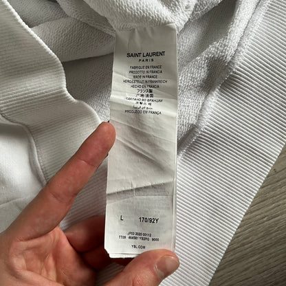 Saint Laurent Small Logo White Hoodie made in France from 100% cotton. Features a minimalist chest logo with “Saint” and “Laurent” separated by a small red square, silver-tipped drawstrings engraved with branding, and a classic front pocket. Designed with the brand’s signature minimalist aesthetic.