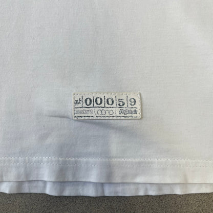Saints Row 2 x PLNY Textylia 2008 White Promo Tee is a rare Poland-exclusive promotional shirt released for Saints Row 2 in collaboration with Polish brand PLNY Textylia, limited to a numbered run (this piece numbered #00059). The front features a black and white Saints Row 2 logo over yellow tribal graphics with a smaller PLNY Textylia logo below, plus a patch displaying both brand logos, while the back carries a large yellow dot/square-style graphic of the game's cover character.