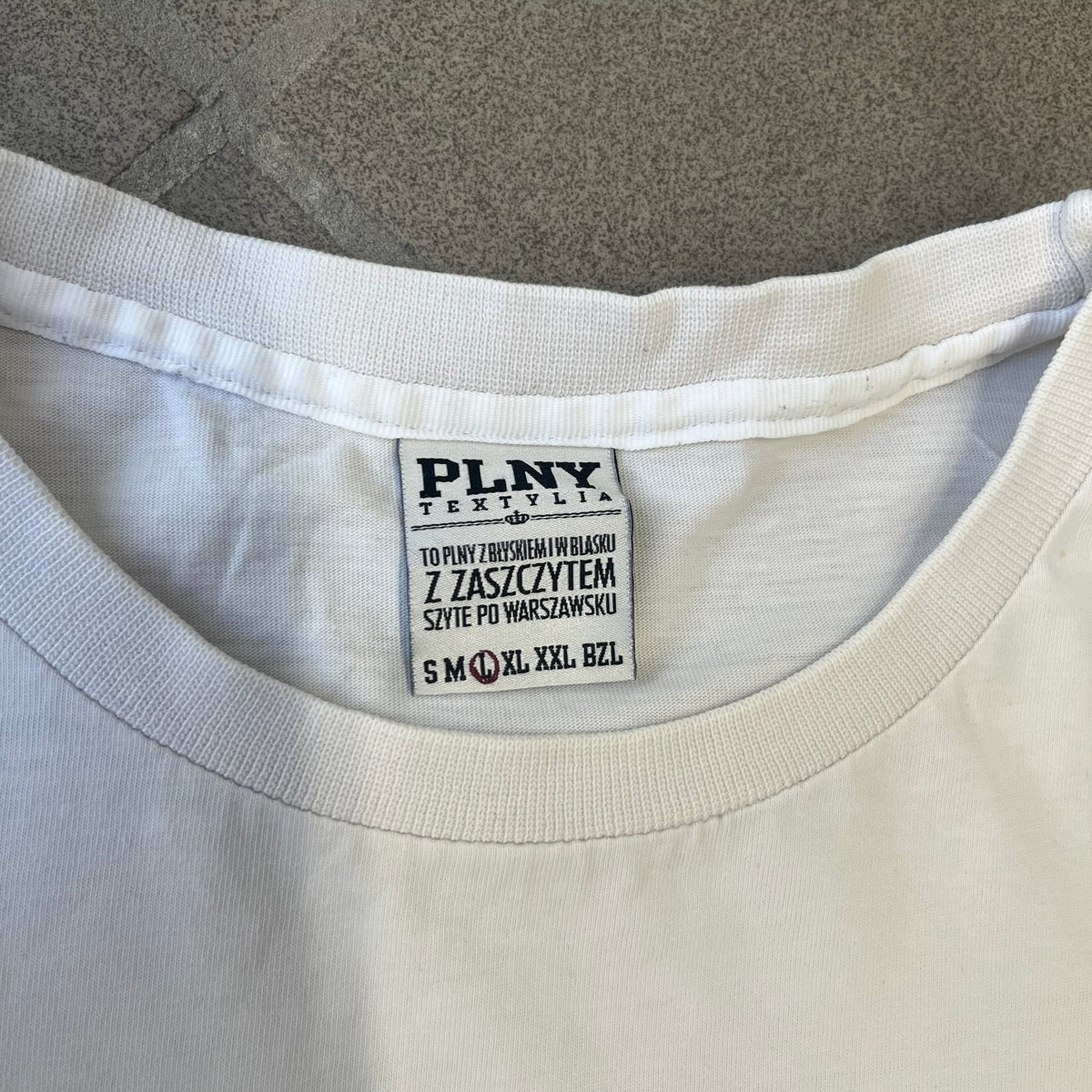 Saints Row 2 x PLNY Textylia 2008 White Promo Tee is a rare Poland-exclusive promotional shirt released for Saints Row 2 in collaboration with Polish brand PLNY Textylia, limited to a numbered run (this piece numbered #00059). The front features a black and white Saints Row 2 logo over yellow tribal graphics with a smaller PLNY Textylia logo below, plus a patch displaying both brand logos, while the back carries a large yellow dot/square-style graphic of the game's cover character.
