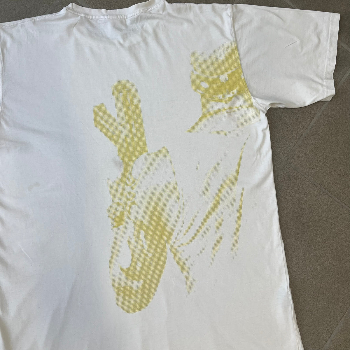Saints Row 2 x PLNY Textylia 2008 White Promo Tee is a rare Poland-exclusive promotional shirt released for Saints Row 2 in collaboration with Polish brand PLNY Textylia, limited to a numbered run (this piece numbered #00059). The front features a black and white Saints Row 2 logo over yellow tribal graphics with a smaller PLNY Textylia logo below, plus a patch displaying both brand logos, while the back carries a large yellow dot/square-style graphic of the game's cover character.