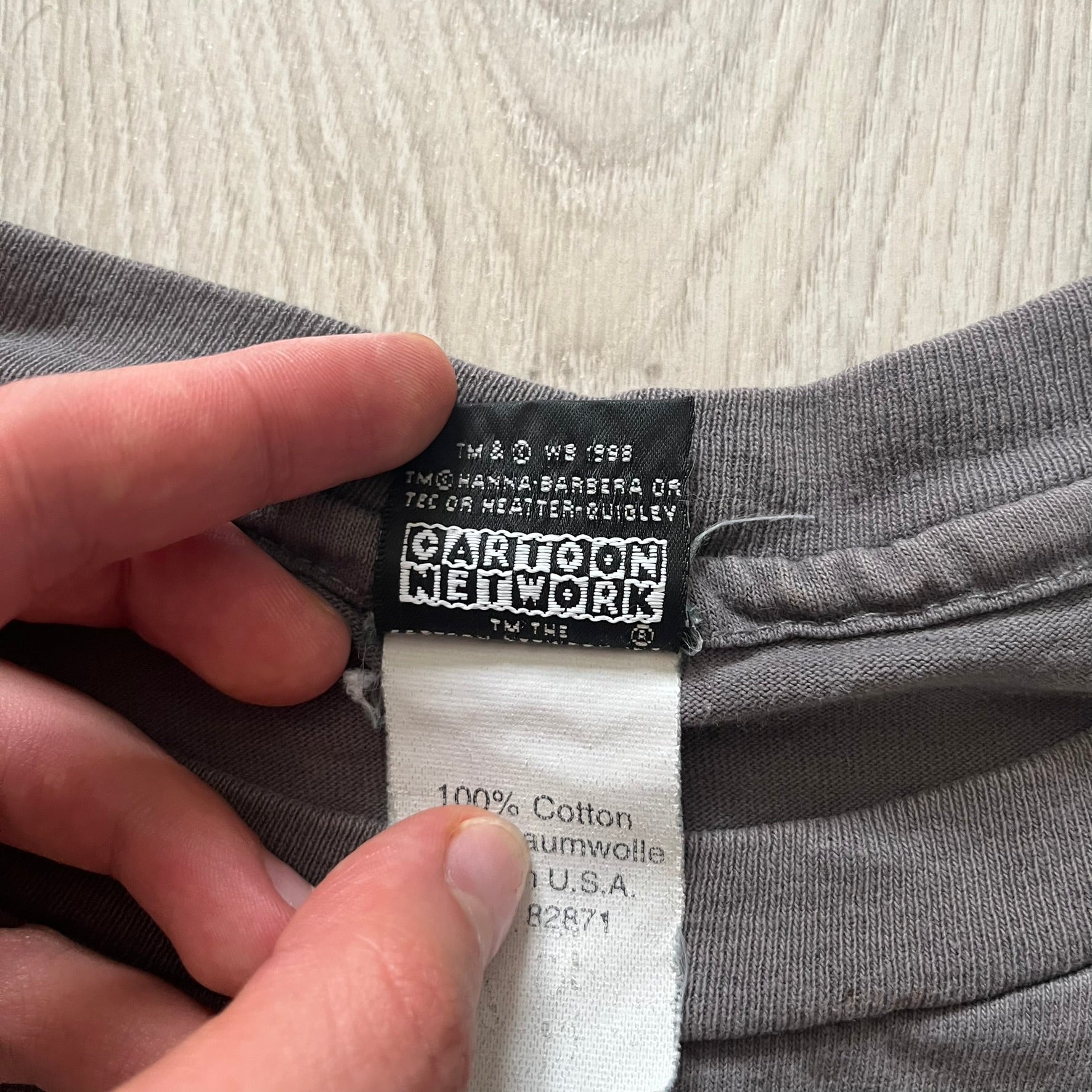 Gray Scooby-Doo tee from 1998, officially licensed by Warner Bros. Studio Store. Graphic shows Scooby emerging through the shirt as if he tore it, paired with classic text. Single-stitch USA-made construction adds authentic vintage charm.