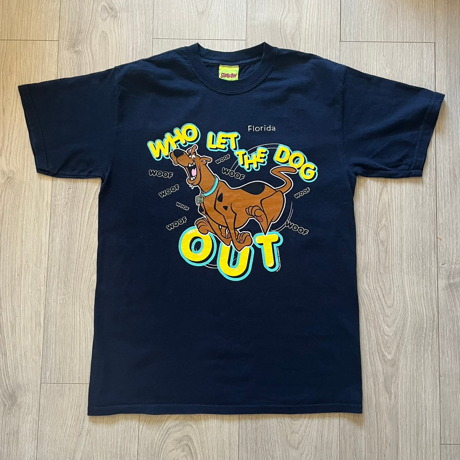 Vintage 2000 Scooby-Doo “Who Let The Dog Out” tee in Navy. Features a big colorful graphic of Scooby running, framed by “Who Let The Dog Out” and playful “Woof” prints. Licensed by Hanna-Barbera with the original green Scooby-Doo tag.