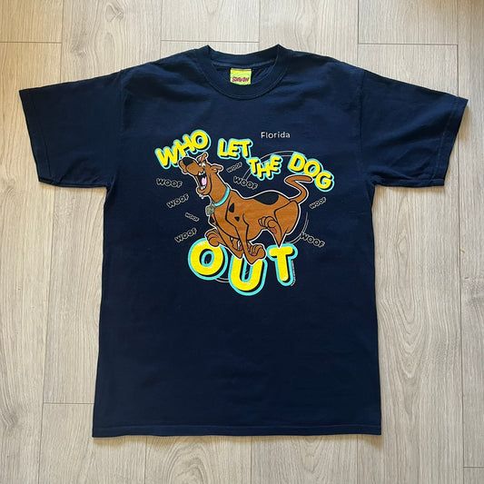 Vintage 2000 Scooby-Doo “Who Let The Dog Out” tee in Navy. Features a big colorful graphic of Scooby running, framed by “Who Let The Dog Out” and playful “Woof” prints. Licensed by Hanna-Barbera with the original green Scooby-Doo tag.