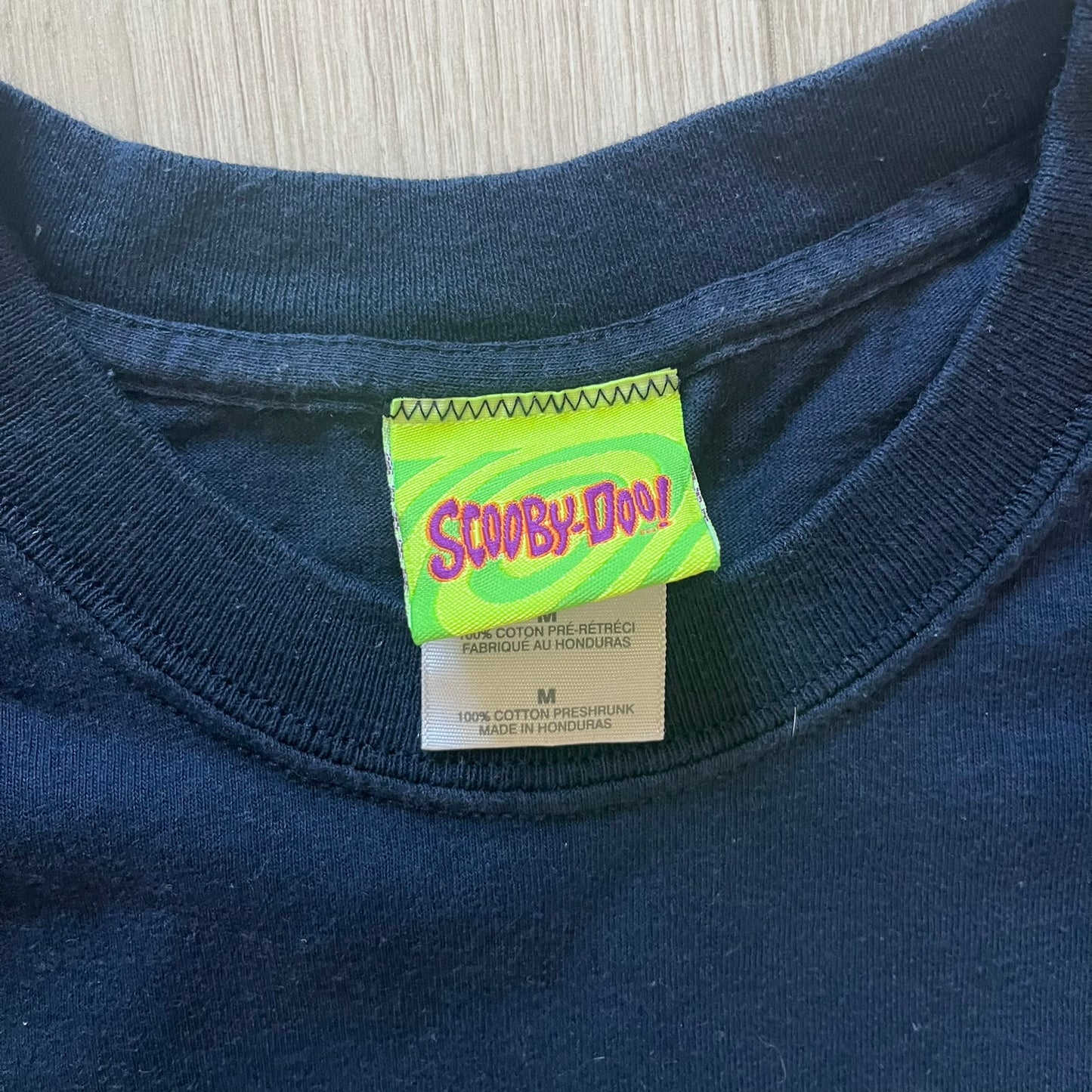 Vintage 2000 Scooby-Doo “Who Let The Dog Out” tee in Navy. Features a big colorful graphic of Scooby running, framed by “Who Let The Dog Out” and playful “Woof” prints. Licensed by Hanna-Barbera with the original green Scooby-Doo tag.