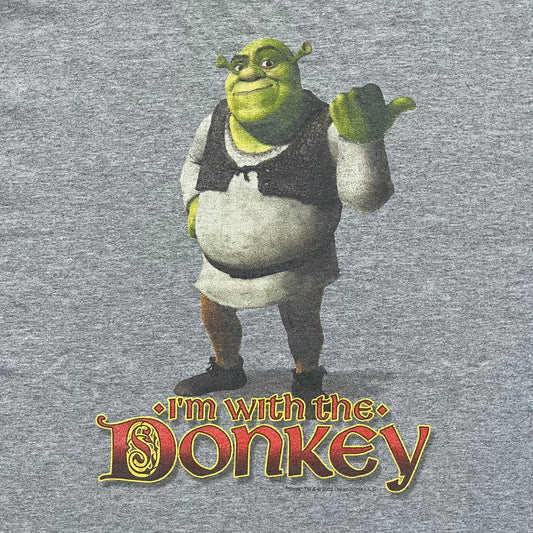 Shrek 2003 “I’m with the Donkey” Gray Tee is a gray T-shirt made from 90% cotton and 10% polyester. The front features Shrek pointing to the side with “I’m with the Donkey” text in a medieval font, and a small DreamWorks Shrek 2003 licensing print below. The neck tag shows Shrek and Universal Studios branding.