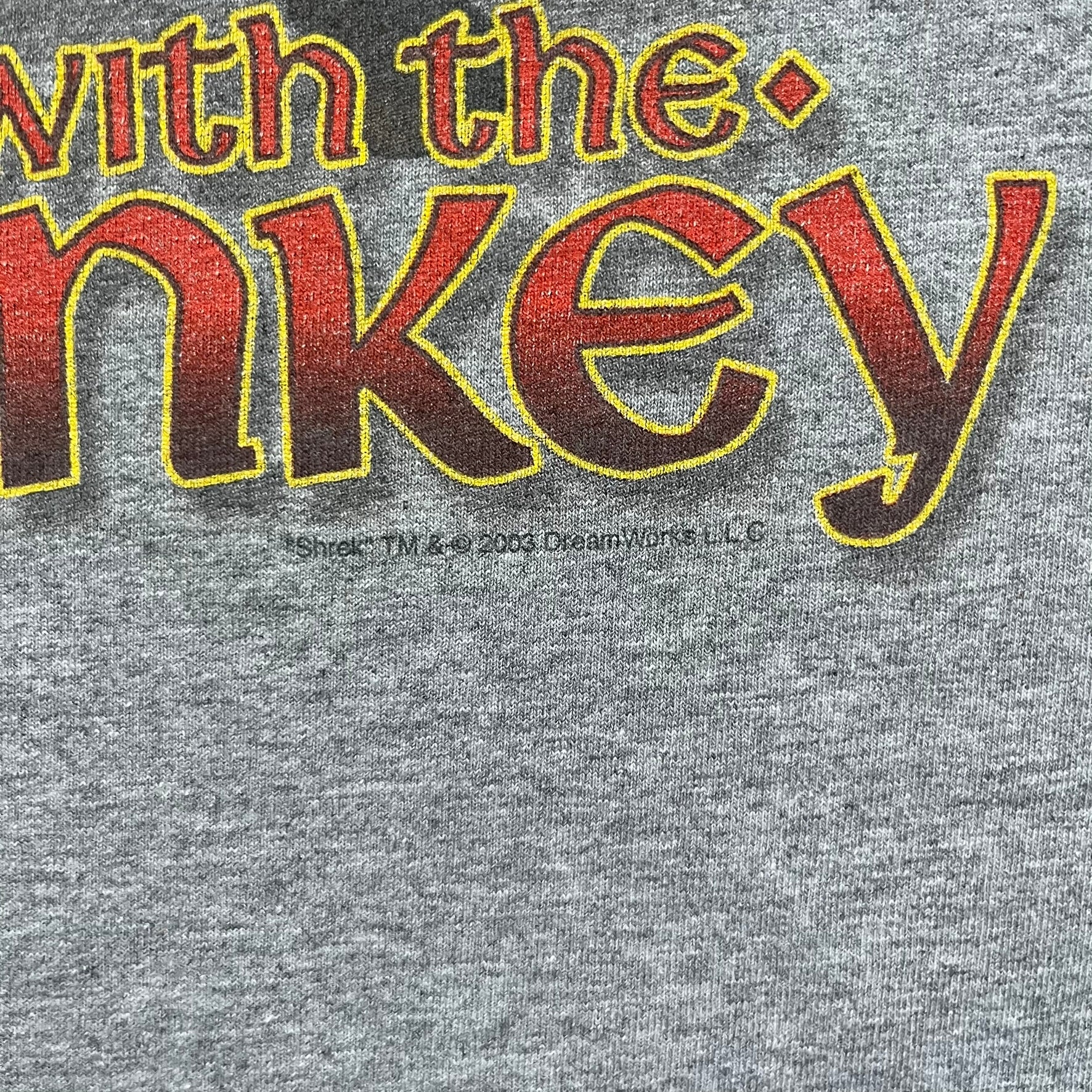 Shrek 2003 “I’m with the Donkey” Gray Tee is a gray T-shirt made from 90% cotton and 10% polyester. The front features Shrek pointing to the side with “I’m with the Donkey” text in a medieval font, and a small DreamWorks Shrek 2003 licensing print below. The neck tag shows Shrek and Universal Studios branding.