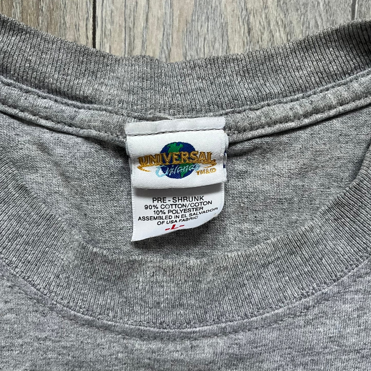 Shrek 2003 “I’m with the Donkey” Gray Tee is a gray T-shirt made from 90% cotton and 10% polyester. The front features Shrek pointing to the side with “I’m with the Donkey” text in a medieval font, and a small DreamWorks Shrek 2003 licensing print below. The neck tag shows Shrek and Universal Studios branding.