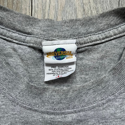 Shrek 2003 “I’m with the Donkey” Gray Tee is a gray T-shirt made from 90% cotton and 10% polyester. The front features Shrek pointing to the side with “I’m with the Donkey” text in a medieval font, and a small DreamWorks Shrek 2003 licensing print below. The neck tag shows Shrek and Universal Studios branding.