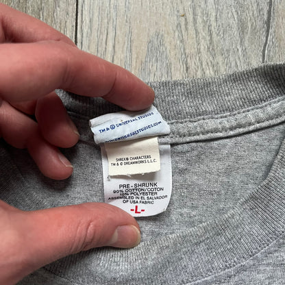 Shrek 2003 “I’m with the Donkey” Gray Tee is a gray T-shirt made from 90% cotton and 10% polyester. The front features Shrek pointing to the side with “I’m with the Donkey” text in a medieval font, and a small DreamWorks Shrek 2003 licensing print below. The neck tag shows Shrek and Universal Studios branding.