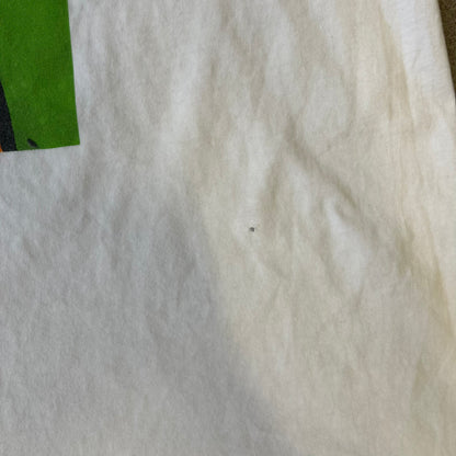 Slawn 2025 White Astroboy Tee is a white T-shirt featuring a rectangular graphic of a yellow Astroboy-inspired figure with a sad Slawn-style face and black hair, set against a green background. It carries a Slawn neck tag.
