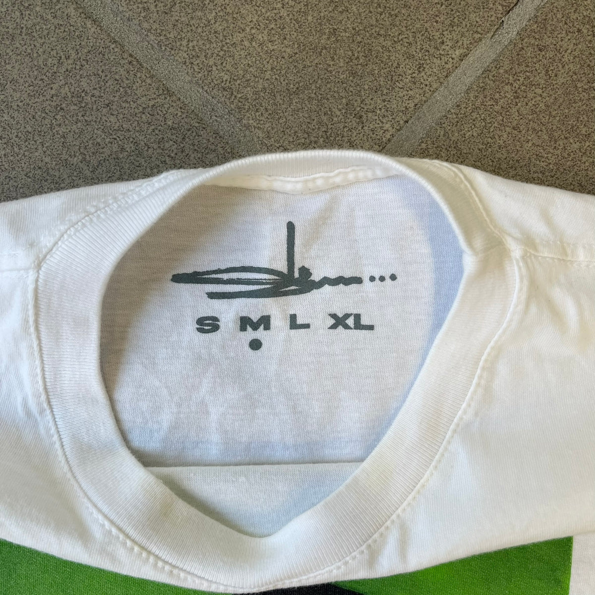 Slawn 2025 White Astroboy Tee is a white T-shirt featuring a rectangular graphic of a yellow Astroboy-inspired figure with a sad Slawn-style face and black hair, set against a green background. It carries a Slawn neck tag.