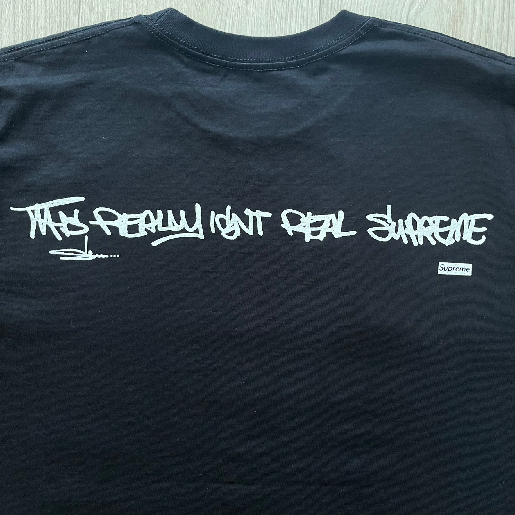 Black Batpreme tee designed by Slawn with Supreme Box Logo and his iconic Batman graphic on the front. Printed neck tag with signature and back shows handwritten-style text saying “This really isn’t real Supreme” with Slawn signature and the Supreme bogo. A rare, art-driven streetwear essential.