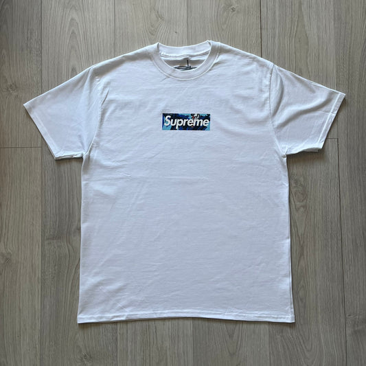 White Slawn Batpreme tee featuring a Batman-inspired graphic with iconic twist by Slawn and Supreme text overlay. Printed neck tag shows Slawn’s signature, while the back reads “This really isn’t real Supreme” in hand-drawn style with signature and logo. A striking, collectible streetwear piece.